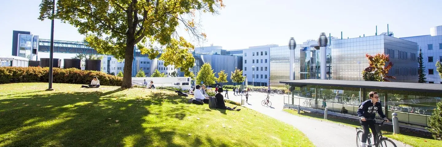 Uitzicht naar de gebouwen op Tampere Campus. Studenten zitten op het gras in de zon