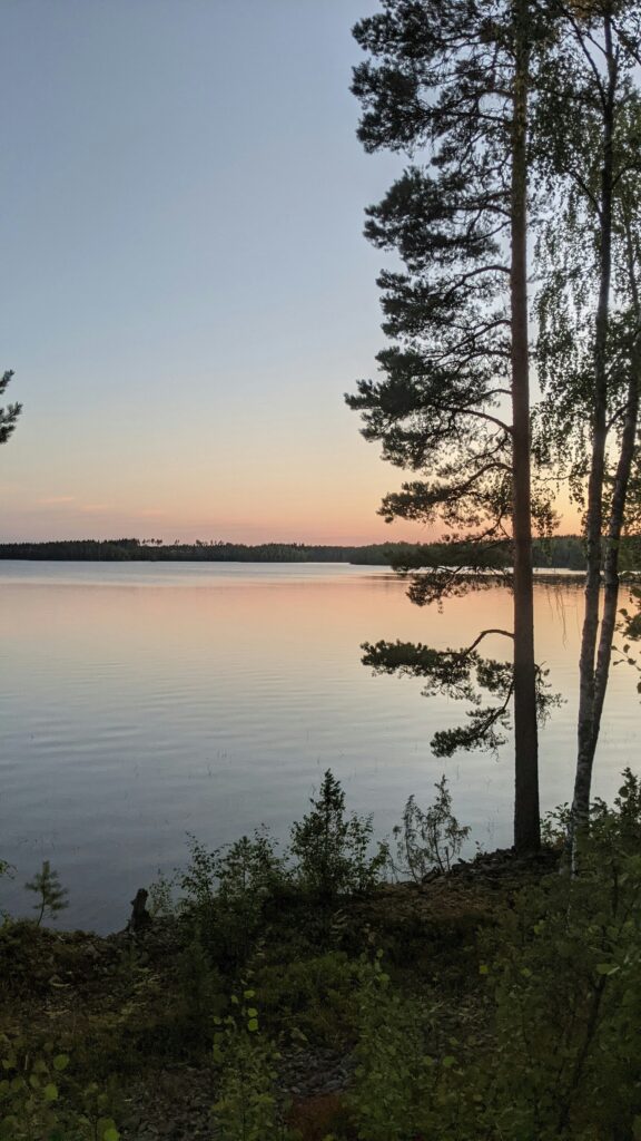 Uitzicht over een meer met bomen in silhouette en een oranje gloed van de ondergaande zon
